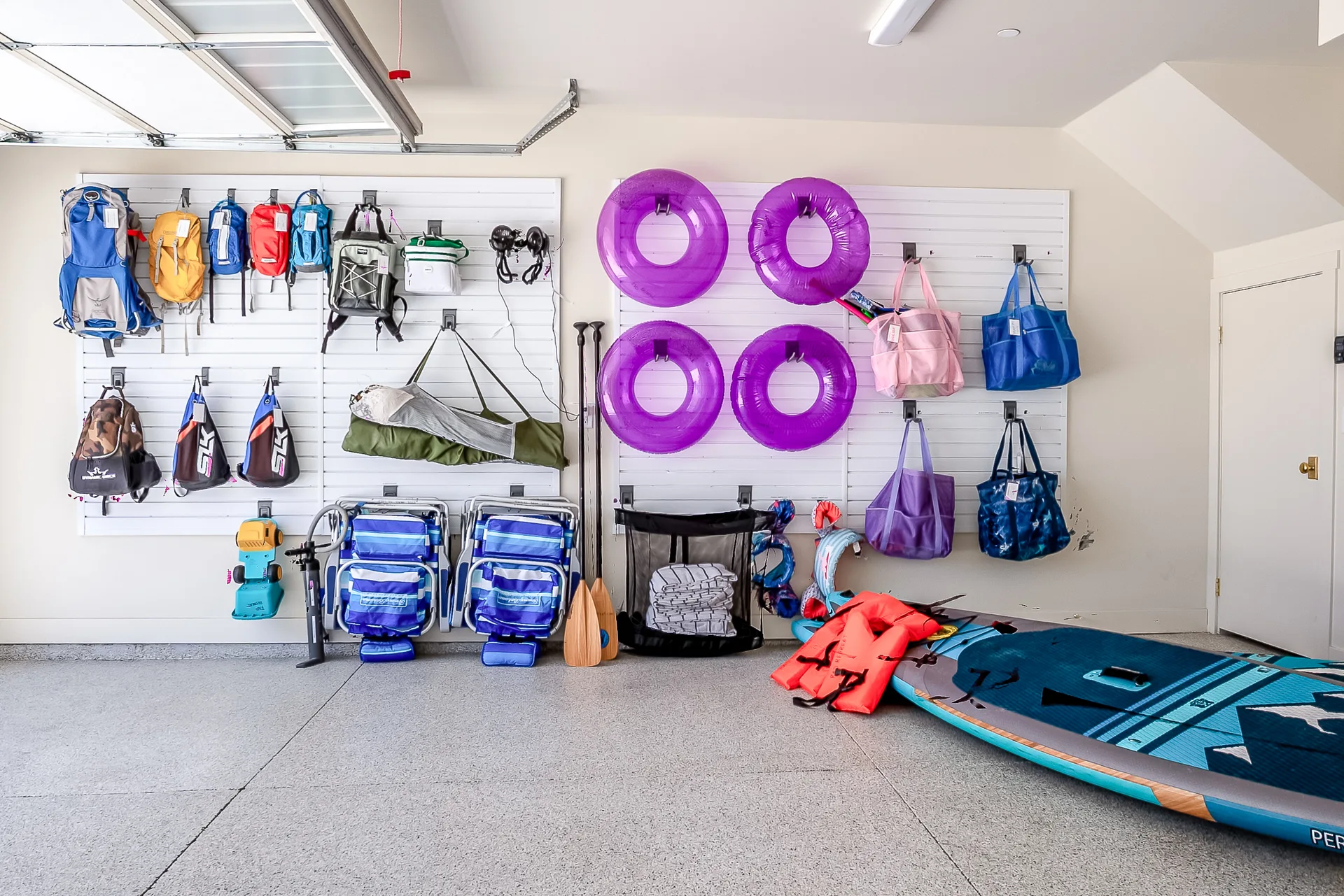 Organized guest gear wall with hydration packs, beach chairs, pool floats, activity bags, and paddleboards
