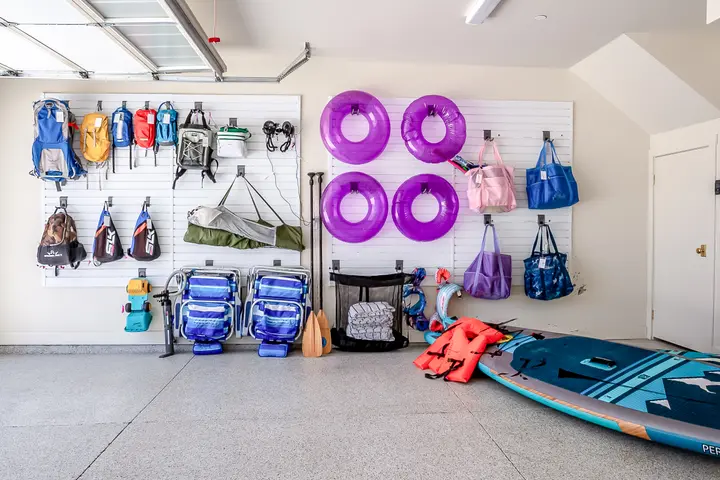 Organized guest gear wall with hydration packs, beach chairs, pool floats, activity bags, and paddleboards